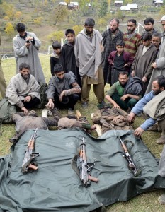 Civilians sit along the bodies of three slain militants and weapons seized from them at Wudur Bala in Kupwara district on Wednesday.—Excelsior/Aabid Nabi
