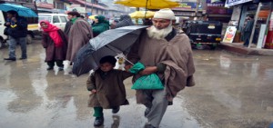 A man gives umbrella cover to a child during rains in Pulwama on Wednesday. -Excelsior/Younis Khaliq